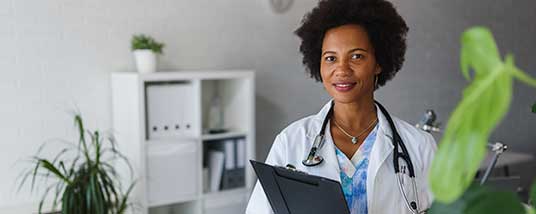 A provider stands in her office with a clipboard, looking assuredly