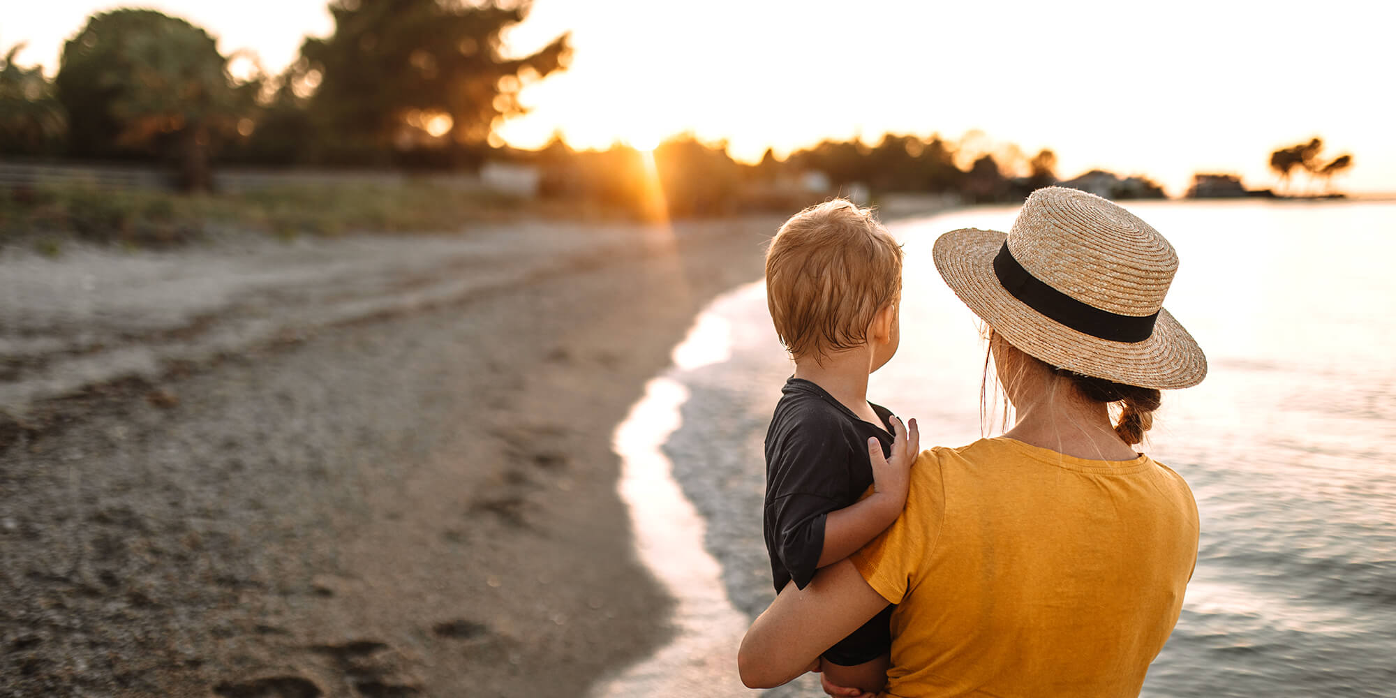 A mother holds her son at the lakeshore and admires the sunset