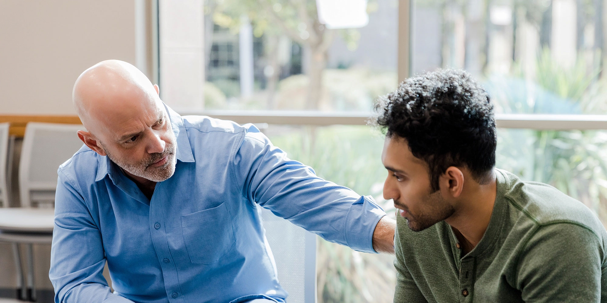 A bald male provider wearing a blue shirt comforts a younger male patient