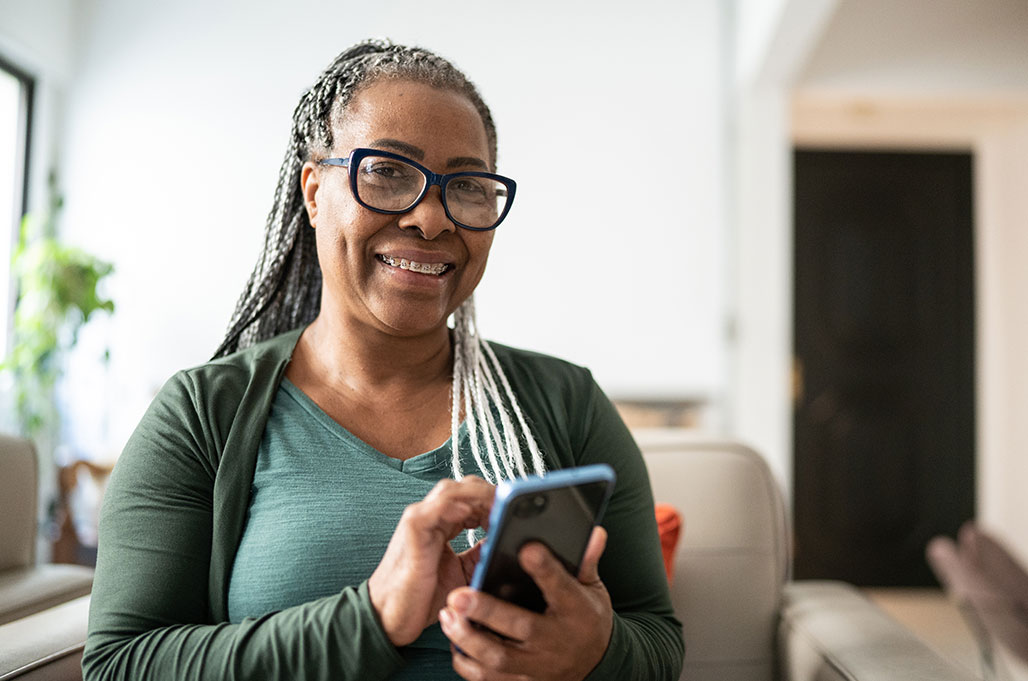 A woman smiles as she taps her phone to contact a physician