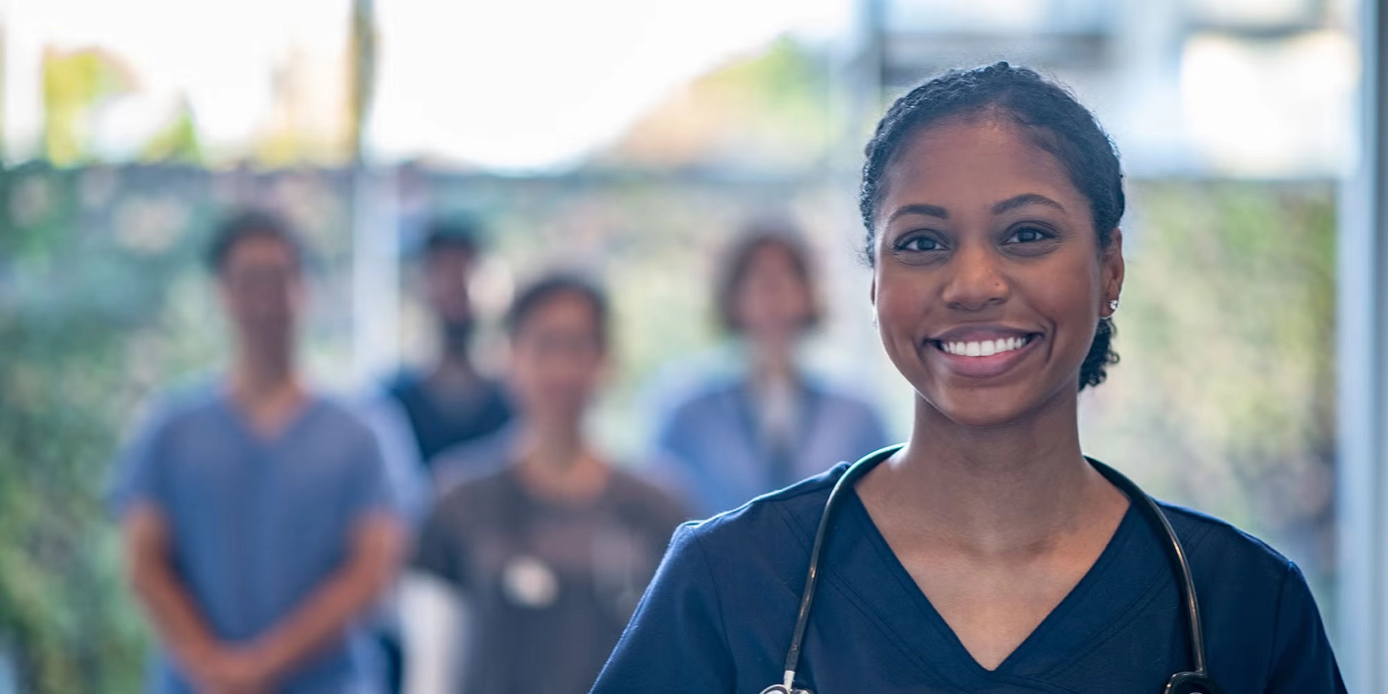 A group of medical residents gathers in a hospital hallway. They're wearing scrubs and one woman stands closer to the camera smiling.