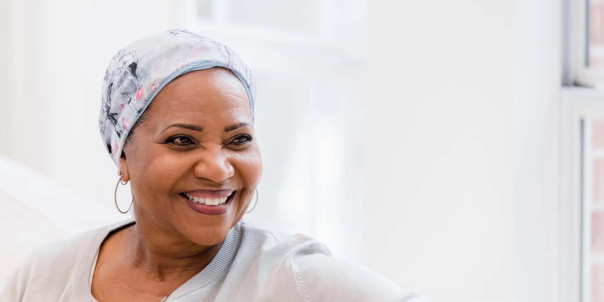 A middle-aged woman smiles off into the distance. She's wearing a scarf on her head as part of her cancer journey.