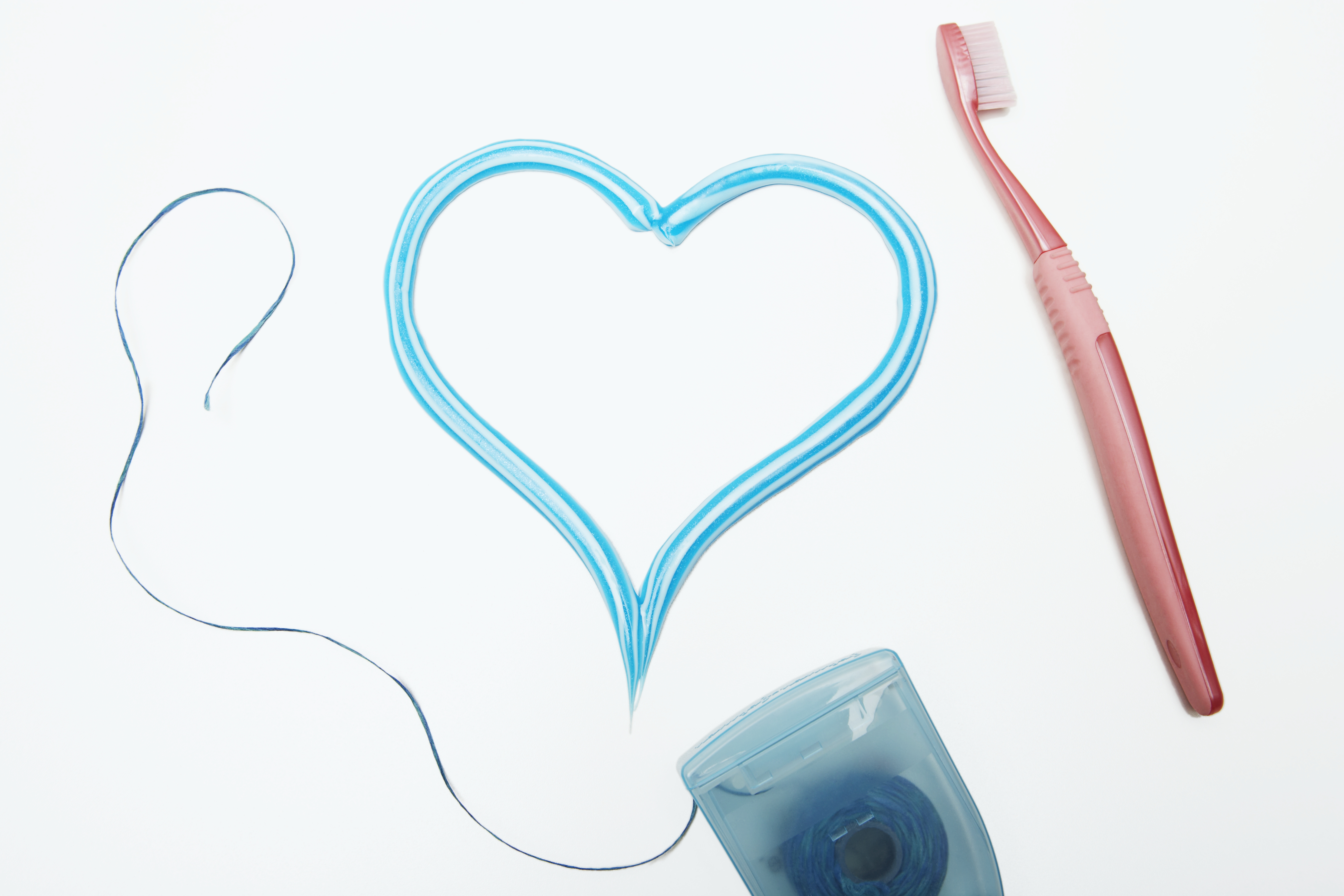 A photo of floss and a toothbrush, with two candy canes touching in the center of the picture to make the shape of a heart