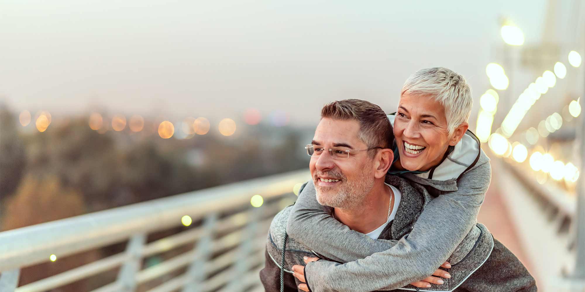 A man gives his partner a piggy back ride along a twinkling path, with the two of them gazing off into the distance, smiling